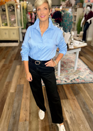 Light blue button-up shirt paired with black belted pants and white loafers in a boutique setting.