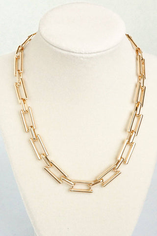 A gold-toned chain necklace with oversized rectangular links, displayed on a white neck mannequin bust against a light gray background.