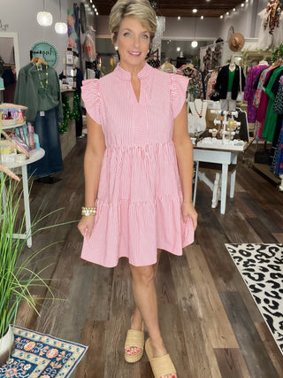 Woman in a pink dress standing in a store with clothing racks and displays.