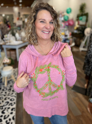 Woman wearing a pink hoodie with a peace symbol design in a store setting
