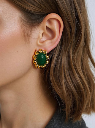 Close-up of a person wearing a gold earring with a green gemstone.
