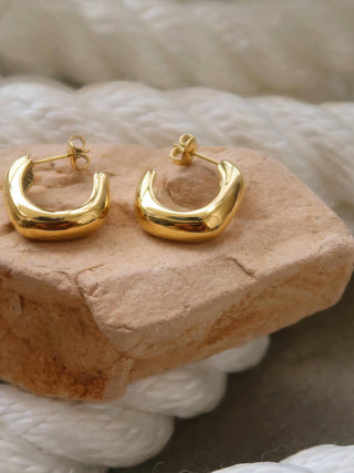 Gold hoop earrings on a textured stone surface