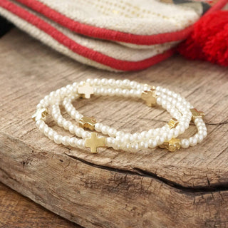 pearl bracelets with side laying golden crosses on a wooden surface with a beige and red bag in the background 