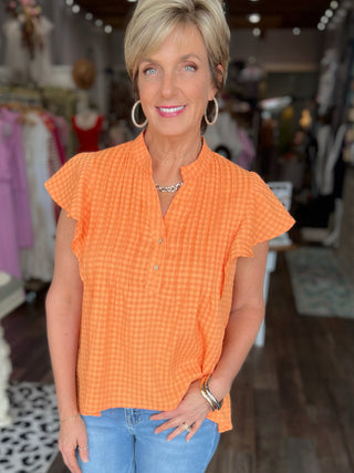Woman wearing an orange checkered blouse and blue jeans in a store setting