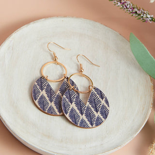 Pair of earrings with gold hoops and blue leaf patterns on a white dish.