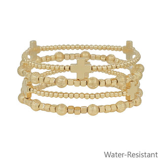 Set of gold beaded bracelets with a cross charm on a white background