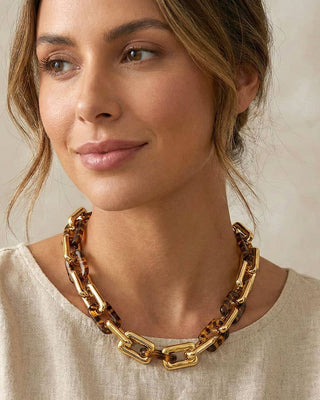 Woman wearing a gold chain necklace against a neutral background