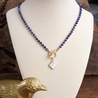 Necklace with blue beads and a white pendant on a mannequin bust, with a gold duck figurine in the foreground.