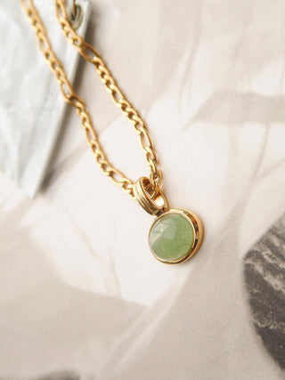 Gold necklace with a green pendant on a neutral background