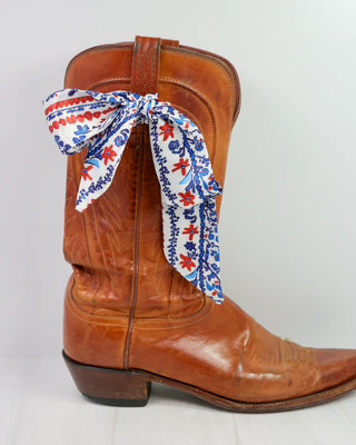 Brown cowboy boot with a colorful bandana tied around it on a white background