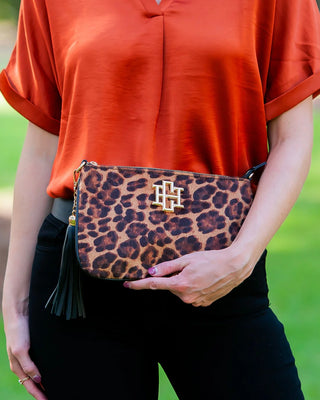 Person holding a leopard print clutch with a gold clasp against a green background