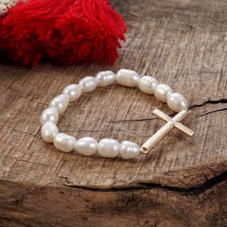 Natural pearl bracelet with a gold cross on a wooden surface with a red tassel in the back 