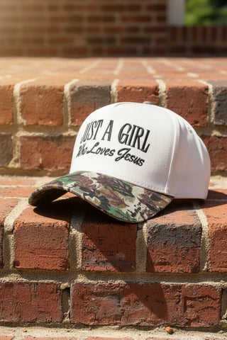 White cap with 'Just a Girl Who Loves Jesus' text and camouflage bill on a white background