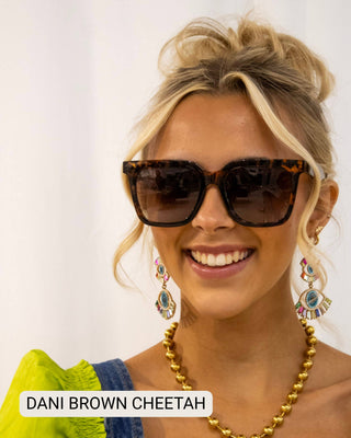 Woman wearing leopard print sunglasses and colorful earrings with a plain background