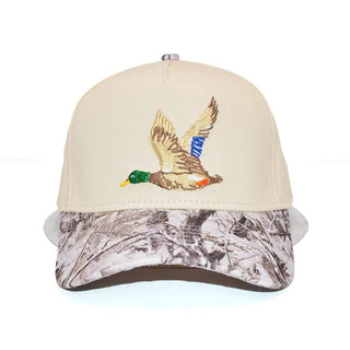 A structured baseball cap with a cream crown and a camouflage-patterned visor. The front features an embroidered flying mallard duck with a green head, brown body, and blue-and-white striped tail.