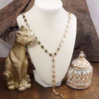 Gold necklace on a mannequin bust with a gold figurine and decorative container on a wooden surface