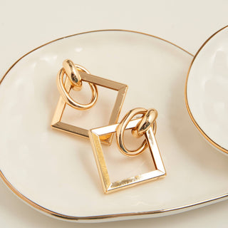 Gold square and circle earrings on a white dish with gold rim
