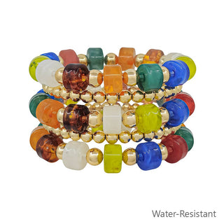 A stack of four colorful beaded stretch bracelets with gold-tone spacer beads, featuring translucent and opaque cube and round beads in blue, green, orange, red, white, and yellow on a white background with 'Water-Resistant' text in the corner.