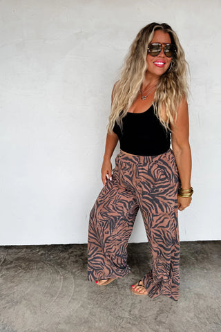 Woman wearing a black top and patterned pants against a white wall.