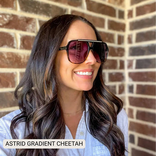 Woman wearing sunglasses with 'Astrid Gradient Cheetah' text against a brick wall