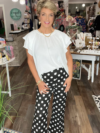 Woman in a store wearing a white top and black polka dot pants.