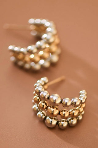 Pair of gold and silver beaded earrings on a brown background