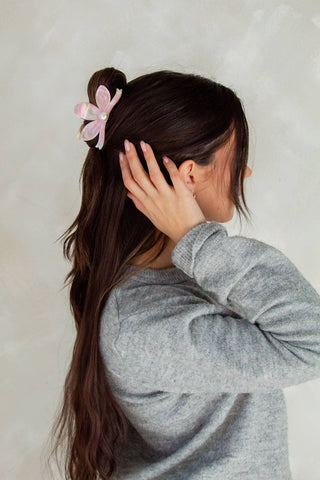 Person with a ponytail and pink flower accessory against a neutral background
