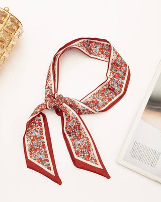 Red floral patterned scarf tied on a white surface with a decorative lamp and magazine in the background.