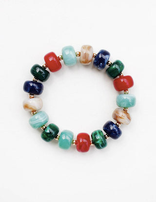 A beaded stretch bracelet featuring glossy, rounded cylindrical beads in multiple colors including red, light blue, dark blue, green, and marbled beige and white, separated by small gold spacer beads, shown on a plain white background.