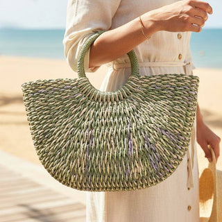 Person holding a green woven handbag on a beach