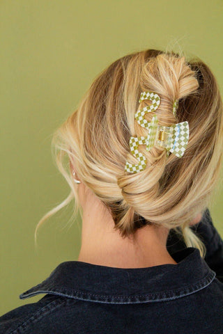 Person with blonde hair styled in an updo with decorative hair clip against a green background