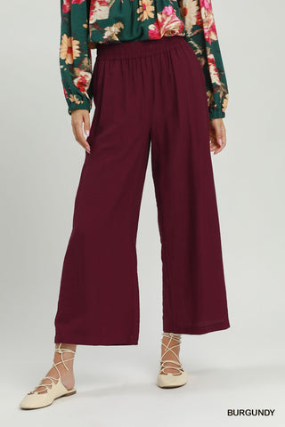 A model is shown from the waist down wearing high-waisted, wide-leg trousers in a deep burgundy color, paired with a green floral blouse and beige lace-up flat sandals. The word 'BURGUNDY' is printed in the bottom right corner.