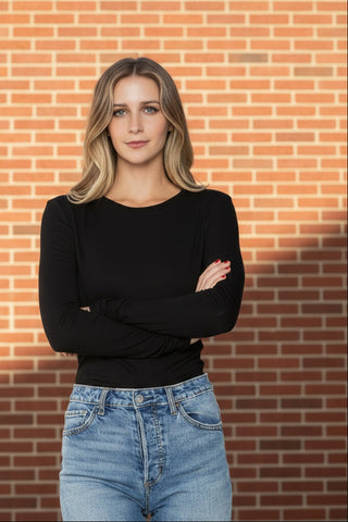 Woman wearing a black long-sleeve top and blue jeans against a white background