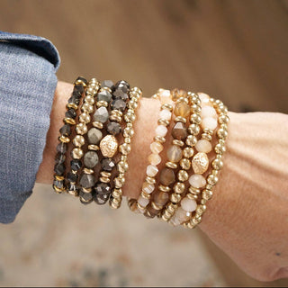 Grey and golden beaded bracelet stack with black pendant accent. 