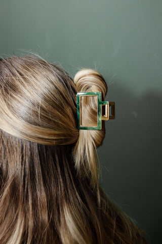 Hair clip with green and gold design in a person's hair against a green background