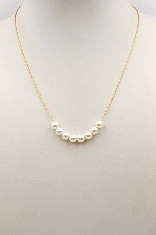 A delicate gold chain necklace featuring a curved row of five white freshwater pearls, displayed on a neutral cream-colored mannequin bust.