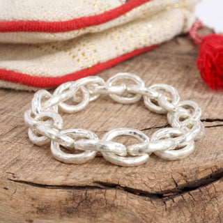 Silver chain bracelet on a wooden surface with a red and beige fabric background