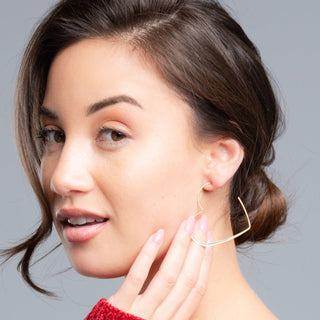 Woman wearing a gold heart hoop earring against a gray background