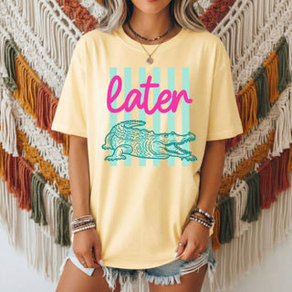 Person wearing a yellow t-shirt with a crocodile graphic and 'later' text in front of a macramé wall.