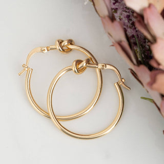 Knotted gold hoop earrings on a light surface with a blurred background