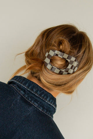 Person with a bun holding a checkered hair clip against a neutral background