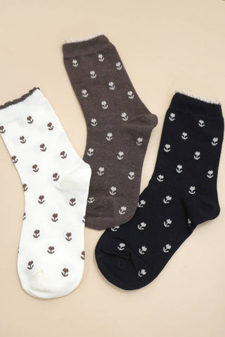 Three pairs of socks in brown and black with small floral patterns on a beige background.