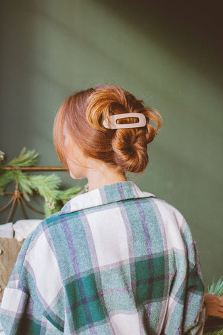 Person with red hair styled in an updo wearing a plaid shirt against a green background