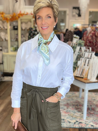 Woman wearing a white shirt and green pants with a scarf in a store setting