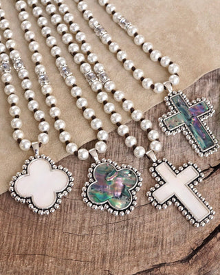 Pearl necklaces with various pendants on a wooden surface