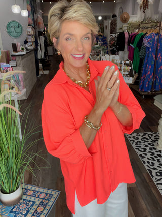 Woman in a bright orange shirt standing in a store with clothing and decor around her.