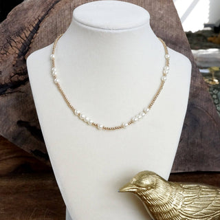 Necklace on a mannequin bust with a gold bird ornament on a wooden surface