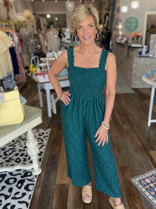 Woman in a teal jumpsuit standing in a store with various items in the background