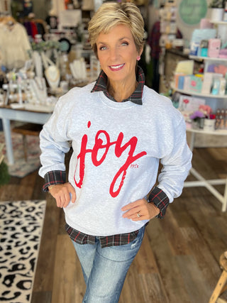 Woman wearing a gray sweatshirt with 'joy' in red text in a store setting