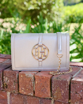 Beige handbag with gold chain on a brick surface with green foliage in the background